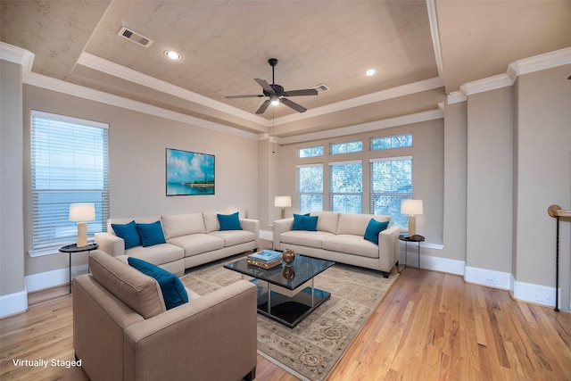 living room featuring visible vents, light wood finished floors, baseboards, a tray ceiling, and crown molding