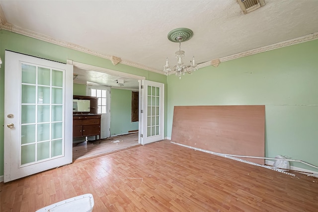 empty room featuring french doors, crown molding, visible vents, wood finished floors, and a chandelier