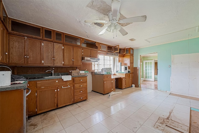 kitchen with a textured ceiling, brown cabinets, and a ceiling fan