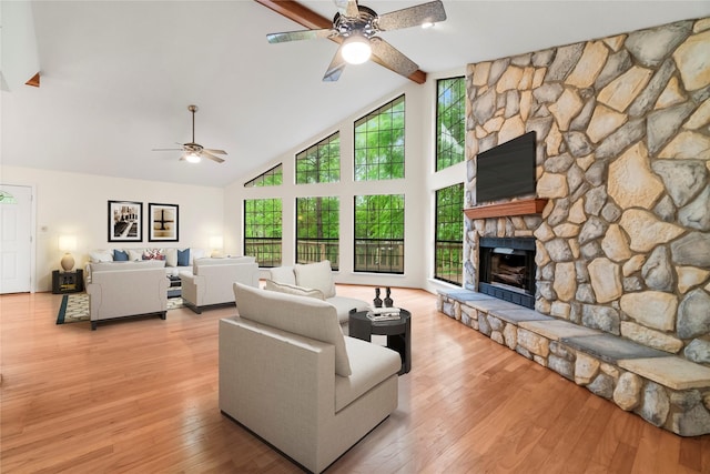 living area featuring light wood-style floors, a ceiling fan, a stone fireplace, high vaulted ceiling, and beamed ceiling