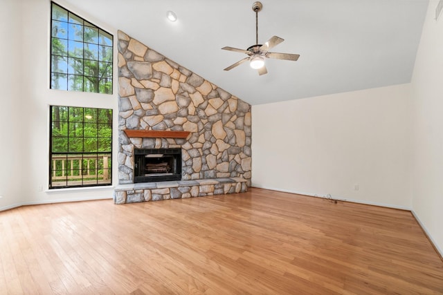 unfurnished living room featuring a ceiling fan, a stone fireplace, wood finished floors, high vaulted ceiling, and baseboards