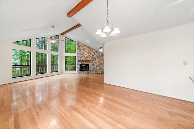 unfurnished living room with wood-type flooring, ceiling fan with notable chandelier, beam ceiling, and a stone fireplace