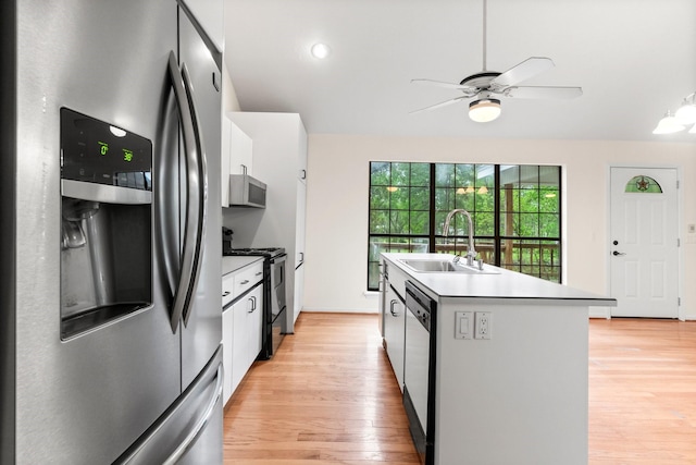 kitchen with light wood finished floors, white cabinets, an island with sink, stainless steel appliances, and a sink