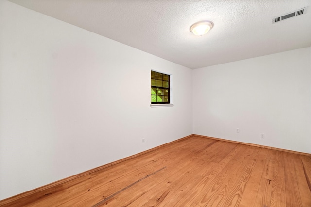 empty room with light wood finished floors, baseboards, visible vents, and a textured ceiling