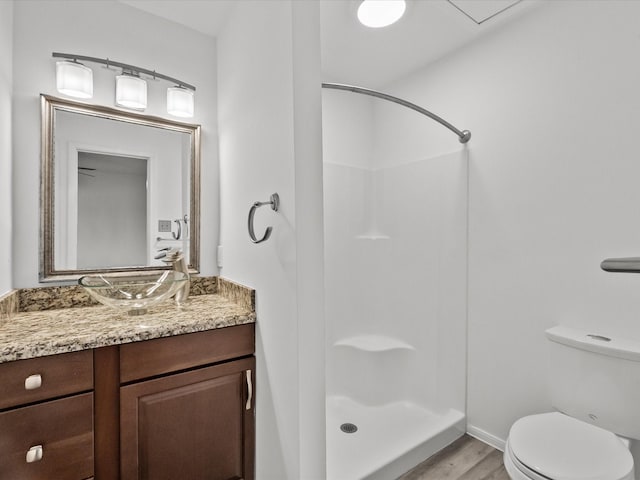 bathroom featuring wood finished floors, toilet, a stall shower, and vanity