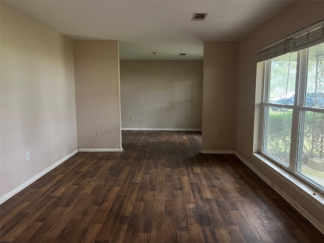 unfurnished room with baseboards, dark wood-style flooring, visible vents, and a healthy amount of sunlight