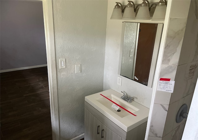 bathroom with a textured wall, vanity, baseboards, and wood finished floors