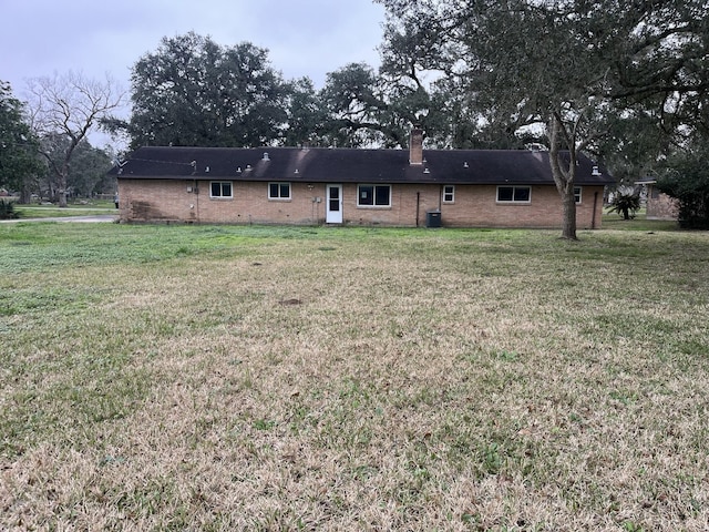 back of house featuring a chimney, central AC, a lawn, and brick siding