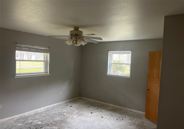 empty room featuring a healthy amount of sunlight, a textured ceiling, baseboards, and a ceiling fan