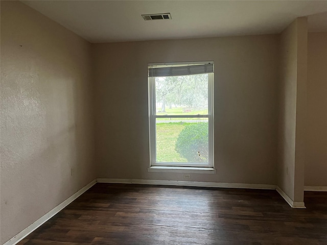 spare room with dark wood-style flooring, visible vents, and baseboards