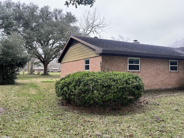 view of side of property featuring brick siding, a lawn, and a chimney