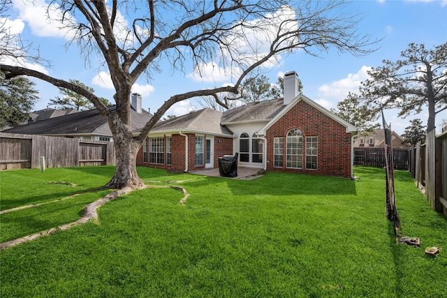 back of property with a lawn, a fenced backyard, brick siding, a chimney, and a patio area