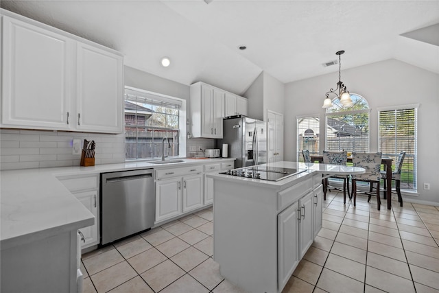 kitchen with light tile patterned floors, a sink, stainless steel appliances, vaulted ceiling, and white cabinets