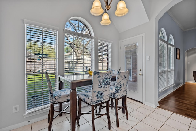 dining space featuring vaulted ceiling, light tile patterned flooring, baseboards, and arched walkways