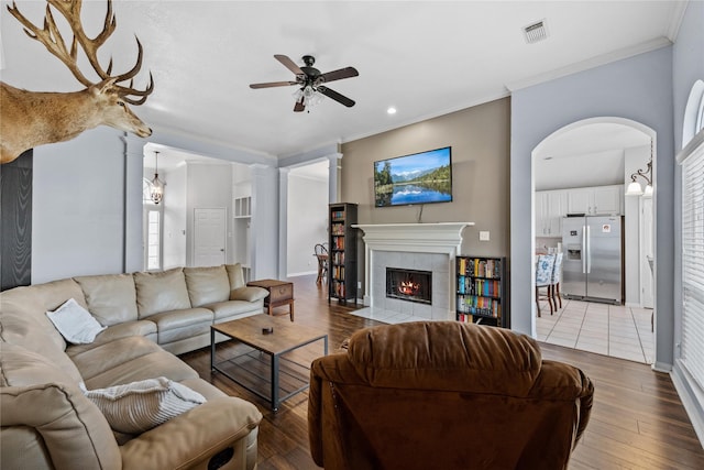 living room with visible vents, crown molding, a tiled fireplace, light wood-style floors, and ornate columns