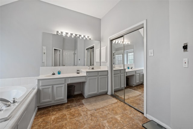 bathroom featuring baseboards, double vanity, a sink, tile patterned floors, and a bath