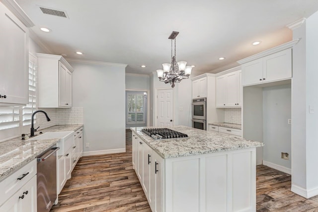 kitchen with crown molding, stainless steel appliances, visible vents, a kitchen island, and a sink