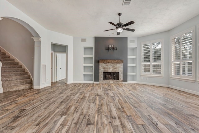 unfurnished living room with a fireplace, wood finished floors, a ceiling fan, visible vents, and built in features