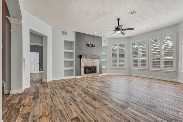 unfurnished living room featuring built in shelves, visible vents, a textured ceiling, wood finished floors, and a tile fireplace