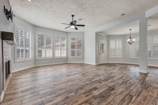 unfurnished living room with ceiling fan with notable chandelier, a fireplace, wood finished floors, and a wealth of natural light