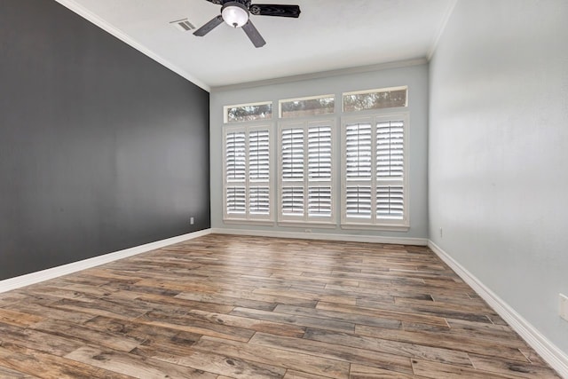 empty room featuring baseboards, wood finished floors, visible vents, and crown molding