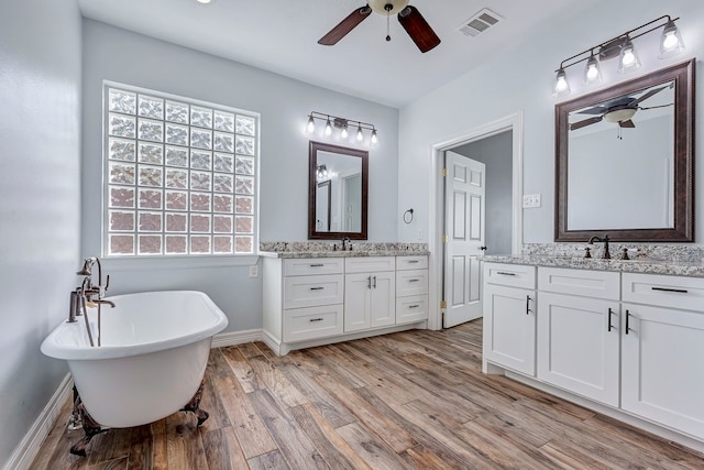 bathroom with visible vents, wood finished floors, a sink, a freestanding bath, and two vanities