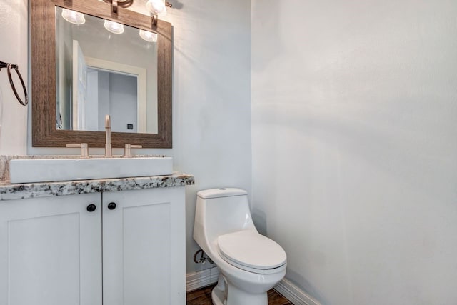 half bath with baseboards, vanity, and toilet