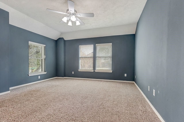 empty room featuring a ceiling fan, carpet flooring, vaulted ceiling, and baseboards