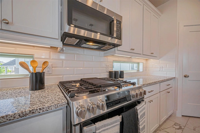 kitchen with light stone countertops, stainless steel appliances, white cabinetry, marble finish floor, and backsplash