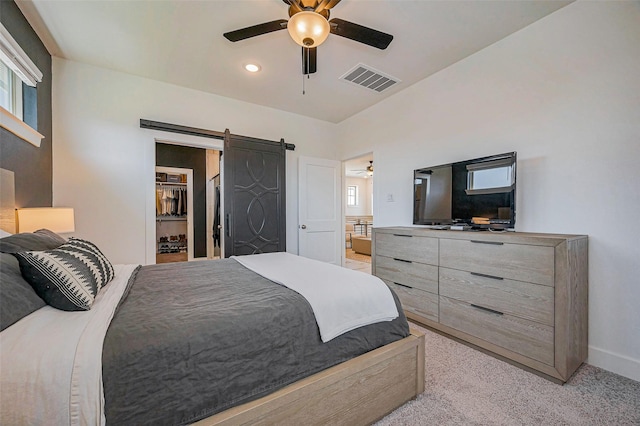 bedroom featuring visible vents, light carpet, a ceiling fan, a barn door, and a spacious closet