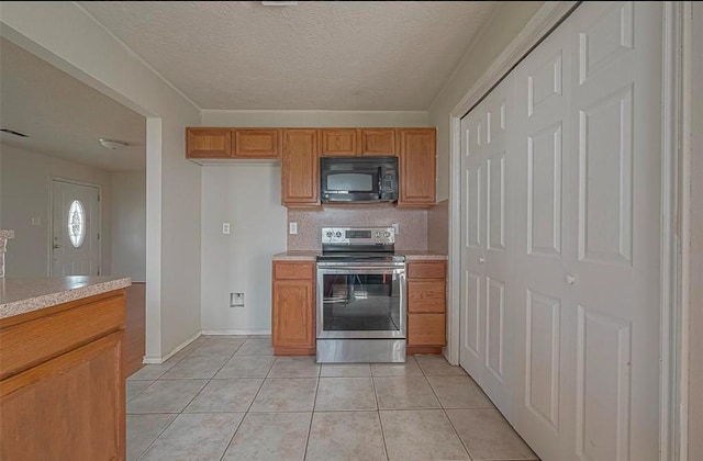 kitchen featuring light countertops, brown cabinetry, light tile patterned flooring, black microwave, and stainless steel electric range