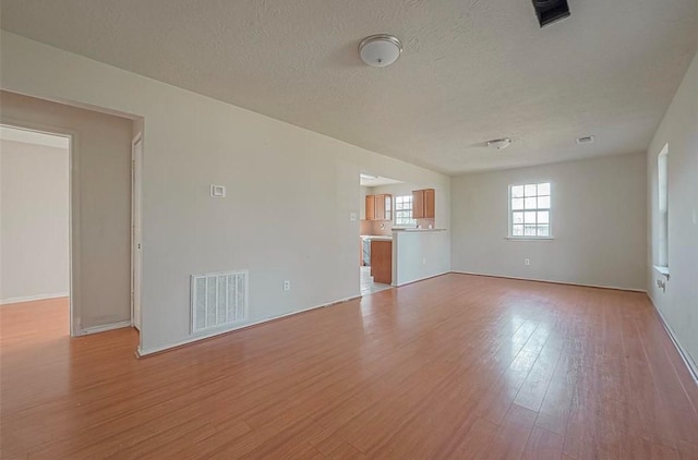 empty room with light wood-style floors, visible vents, and a textured ceiling