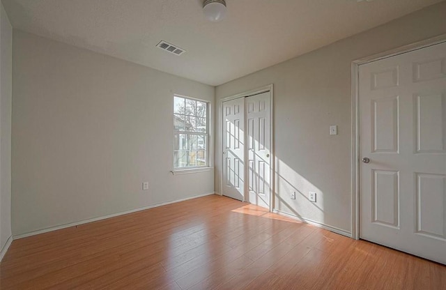 unfurnished bedroom featuring baseboards, a closet, visible vents, and wood finished floors