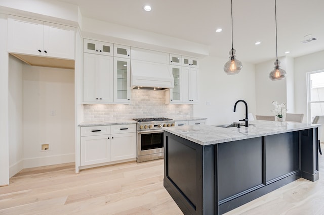 kitchen with premium range hood, a sink, white cabinets, high end stainless steel range oven, and light stone countertops