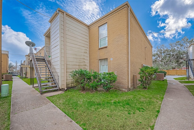 view of side of property featuring cooling unit, brick siding, a yard, and stairway