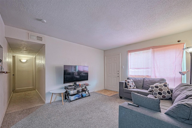 living room with a textured ceiling, carpet flooring, visible vents, and baseboards