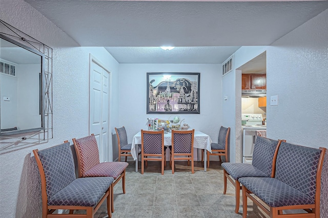 dining area featuring a textured wall, visible vents, a textured ceiling, and stone finish flooring