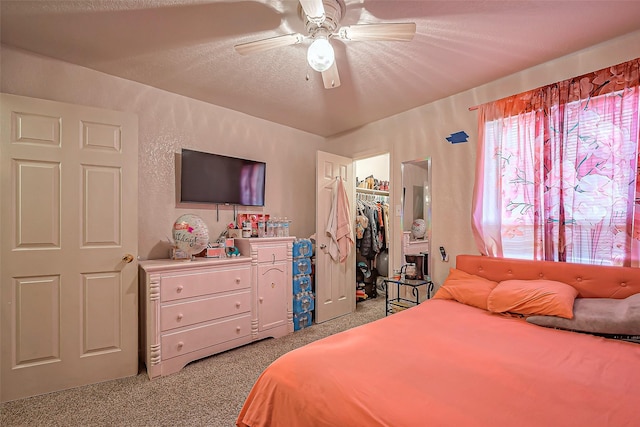 carpeted bedroom with a ceiling fan, a textured wall, a spacious closet, a textured ceiling, and a closet