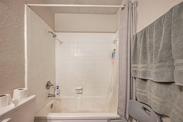 bathroom featuring a textured wall, toilet, and shower / bathtub combination with curtain
