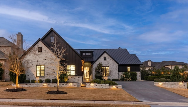 modern farmhouse style home with metal roof, aphalt driveway, stone siding, board and batten siding, and a standing seam roof