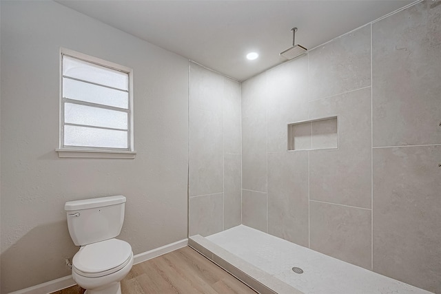 bathroom featuring baseboards, a tile shower, toilet, and wood finished floors