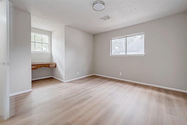 unfurnished room featuring light wood-type flooring, baseboards, visible vents, and a textured ceiling