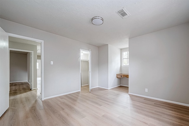 unfurnished room with light wood finished floors, baseboards, visible vents, and a textured ceiling