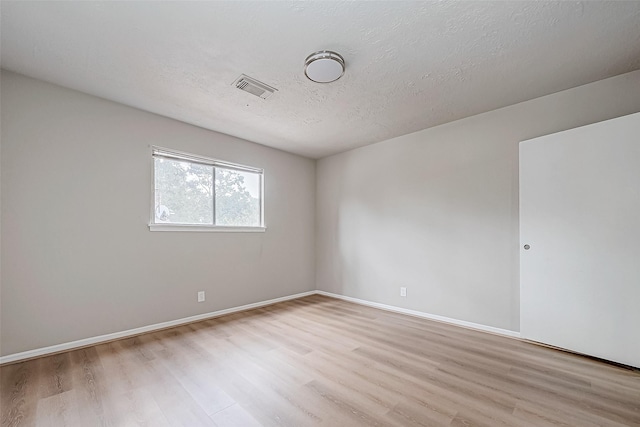 unfurnished room with light wood finished floors, baseboards, visible vents, and a textured ceiling