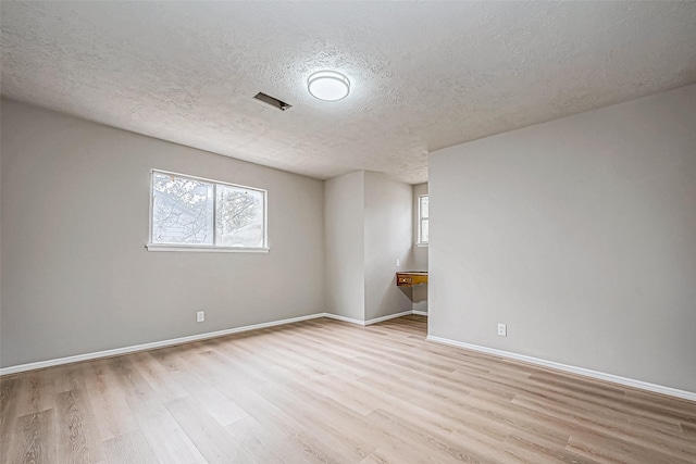 spare room with light wood finished floors, baseboards, and a textured ceiling