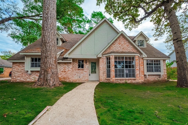 tudor-style house with a front lawn, roof with shingles, and brick siding