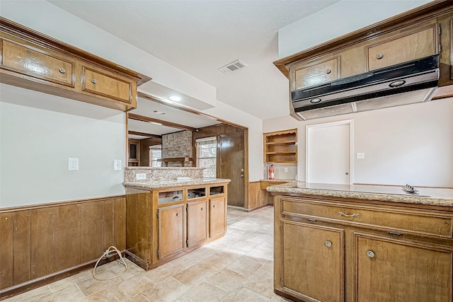 kitchen featuring a wainscoted wall, brown cabinets, visible vents, and under cabinet range hood