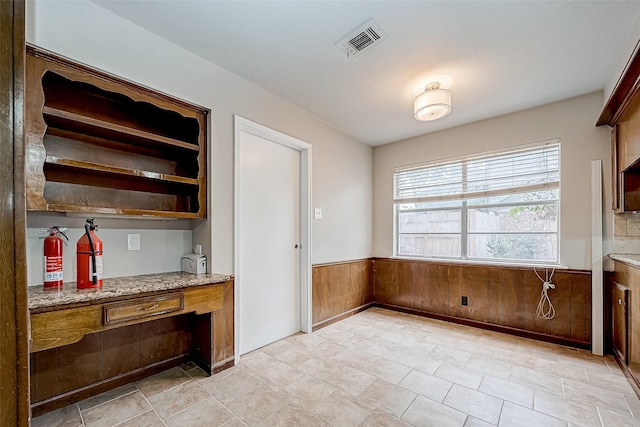 kitchen with wooden walls, visible vents, built in study area, wainscoting, and light stone countertops