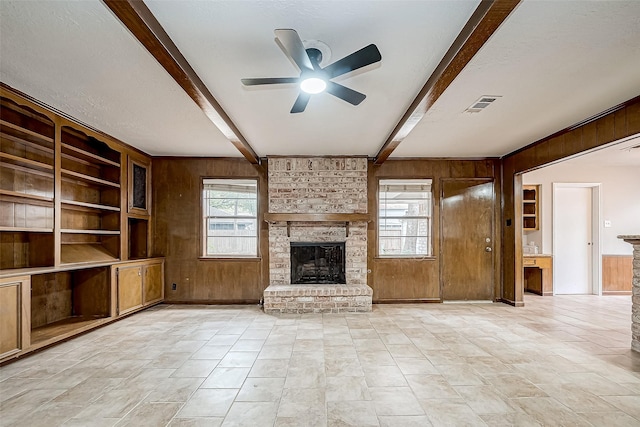 unfurnished living room featuring visible vents, wood walls, and beamed ceiling