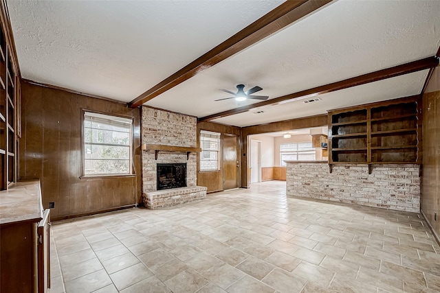 unfurnished living room with a textured ceiling, a brick fireplace, beam ceiling, and wooden walls